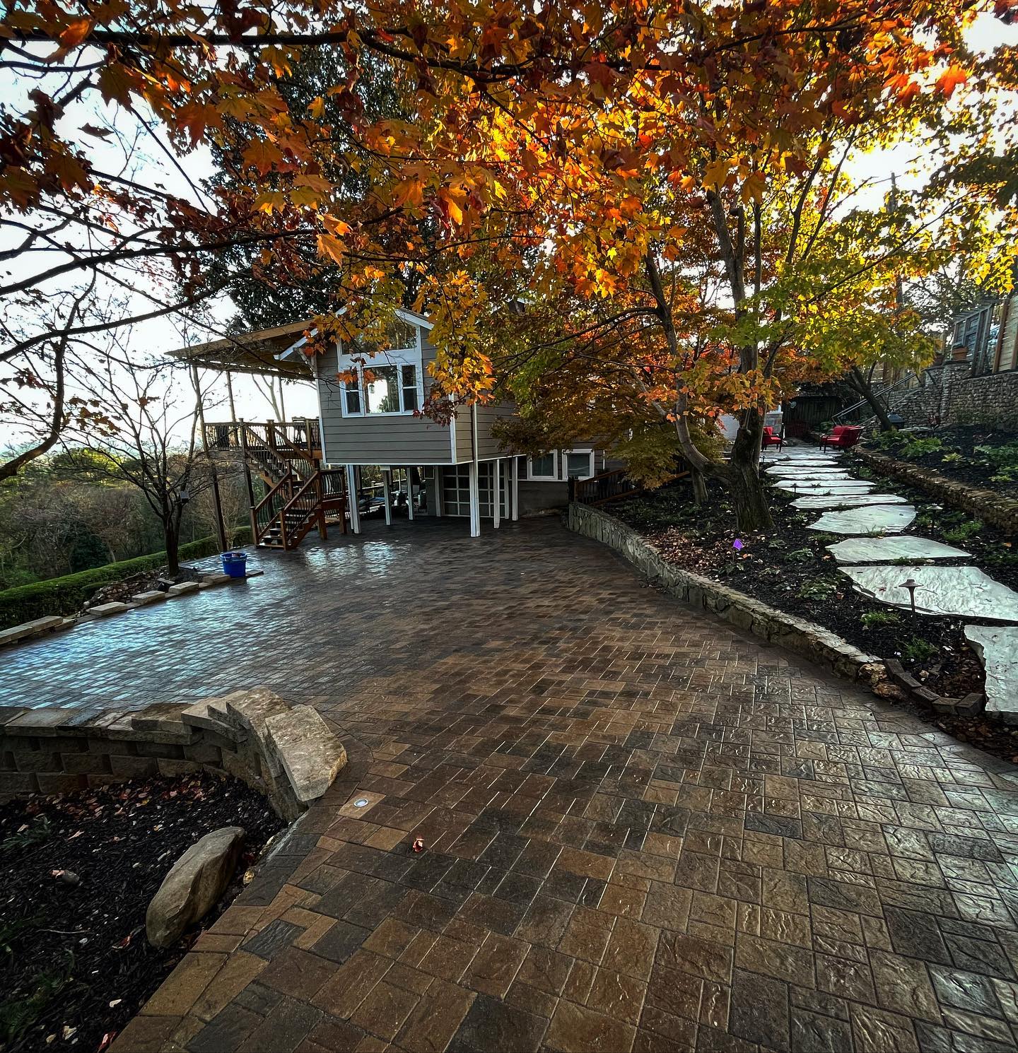 Large patio behind house with retaining wall and stone path surrounded by native trees